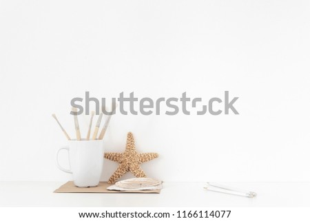 Background with stationary, seashells, sea star, mug, painting brusheson, pencils on white wall background, soft home decor. Copy space for text. Empty space for lettering. Back to shool