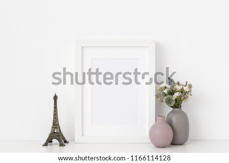 White a5 portrait frame mockup with dried field wild flowers, vases and Eiffel Tower on and white wall background. Empty frame, poster mock up for presentation design. Template frame for text