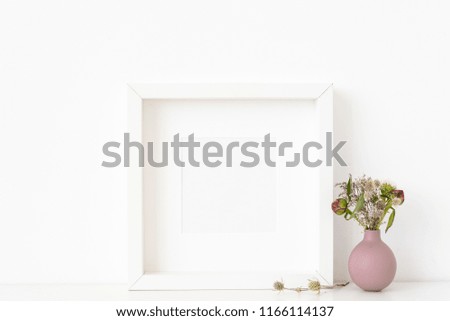 White square portrait frame mockup with dried field wild flowers in vase on white wall background. Empty frame, poster mock up for presentation design. Template frame for text, lettering, modern art.