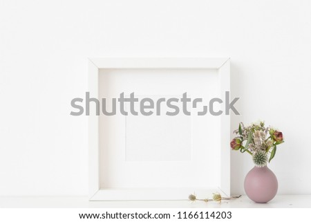 White square portrait frame mockup with dried field wild flowers in vase on white wall background. Empty frame, poster mock up for presentation design. Template frame for text, lettering, modern art.