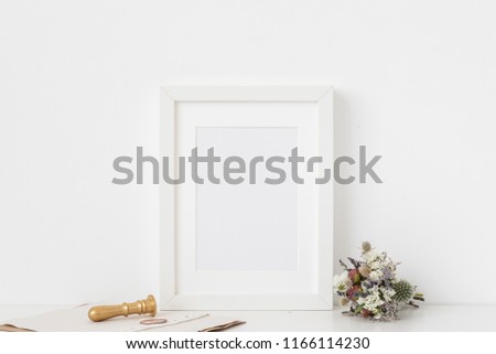 Cute white a5 portrait frame mockup with bouquet of dried flowers, gold stamp and printing on white wall background. Empty frame, poster mock up for presentation design. Template frame for text