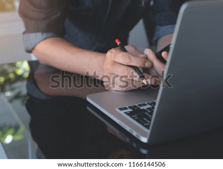 Business man holding pencil using mobile phone and busy working on laptop computer with reflection on office desk. Freelance, creative designer online working from home office.