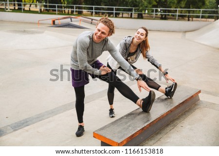 Image of caucasian sporty couple man and woman 20s in sportswear working out and stretching body in skate park