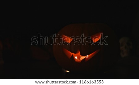 Carved Halloween pumpkin lights inside with flame and skuls around on a black background.
