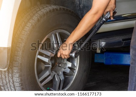 Man hand changing tire of the car by torque wrench in workshop service station.