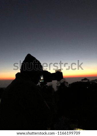 Silhouette view of photographer taking landscape picture by DSLR camera in golden hours.