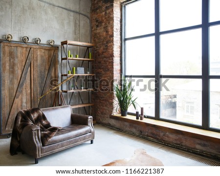 brutal interior in a dark brown color with a leather sofa and large window. Loft style room Royalty-Free Stock Photo #1166221387