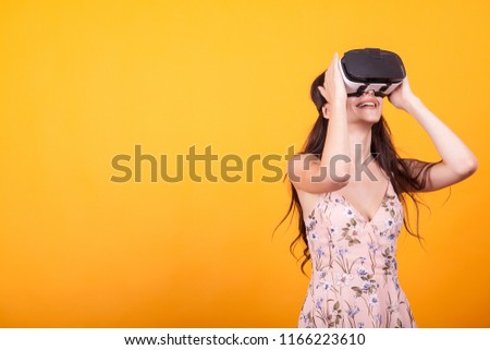 Girl plays vr game in virtual reality helmet in studio over yellow background. Studio portrait of girl playing mobile app on VR Glasses.