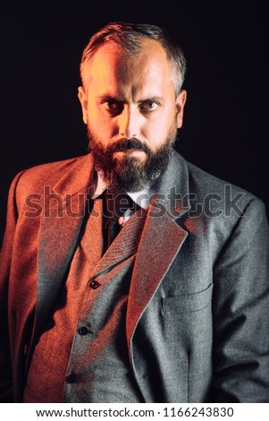 Portrait on a bearded angry looking man boss in suit on black background