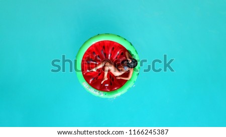 Aerial drone top photo of unidentified woman wearing a hat sitting in inflatable watermelon in deep cyan calm waters like a pool