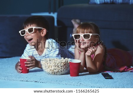 Cute children in 3d glasses watching movie on carpet in evening