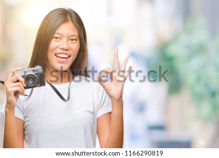 Young asian woman holding vintagera photo camera over isolated background doing ok sign with fingers, excellent symbol