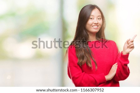 Young asian woman wearing winter sweater over isolated background with a big smile on face, pointing with hand and finger to the side looking at the camera.