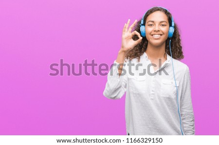 Young hispanic woman wearing headphones doing ok sign with fingers, excellent symbol