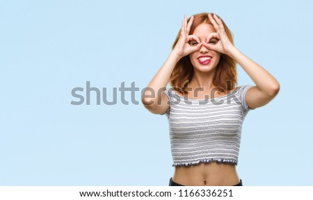 Young beautiful woman over isolated background doing ok gesture like binoculars sticking tongue out, eyes looking through fingers. Crazy expression.