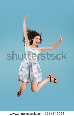 Freedom in moving. Mid-air shot of pretty happy young woman jumping and gesturing against blue studio background. Runnin girl in motion or movement. Human emotions and facial expressions concept