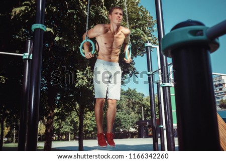 The fit athlete doing exercises at stadium. Caucasian young man outdoor at park at city. Pull up sport exercises. The sport, fitness, health, lifestyle concept
