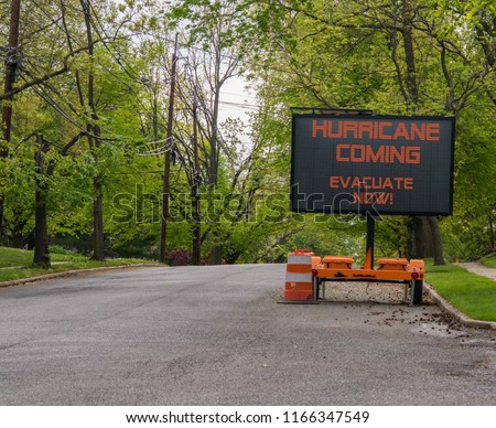 Hurricane Coming Evacuate Now warning information sign on trailer with LED face on suburban street lined with trees Royalty-Free Stock Photo #1166347549