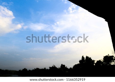 Blue sky background with clouds and have dark tree and wood around picture.