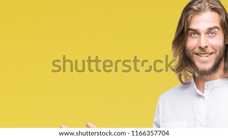 Young handsome man with long hair over isolated background amazed and smiling to the camera while presenting with hand and pointing with finger.