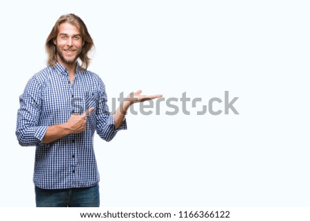 Young handsome man with long hair over isolated background amazed and smiling to the camera while presenting with hand and pointing with finger.