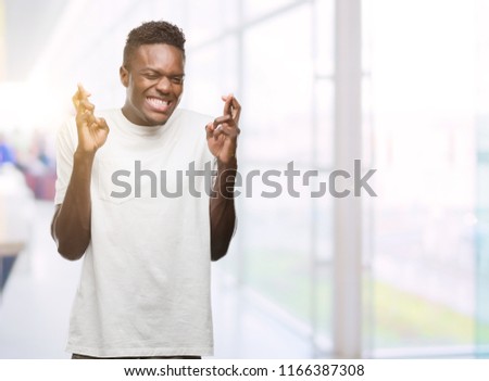 Young african american man wearing white t-shirt smiling crossing fingers with hope and eyes closed. Luck and superstitious concept.