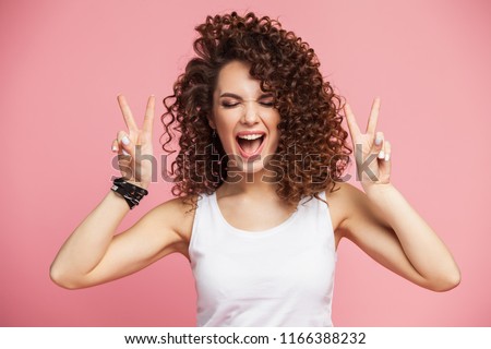 Image of happy young woman standing isolated over pink background showing peace gesture. Looking camera. Royalty-Free Stock Photo #1166388232