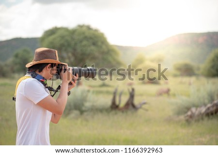 Young man traveler and photographer taking photo of wildlife animal in African safari. Wildlife photography concept Royalty-Free Stock Photo #1166392963