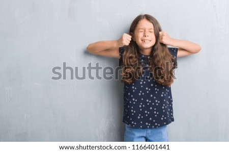 Young hispanic kid over grunge grey wall excited for success with arms raised celebrating victory smiling. Winner concept.