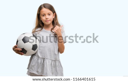 Brunette hispanic girl holding soccer football ball happy with big smile doing ok sign, thumb up with fingers, excellent sign