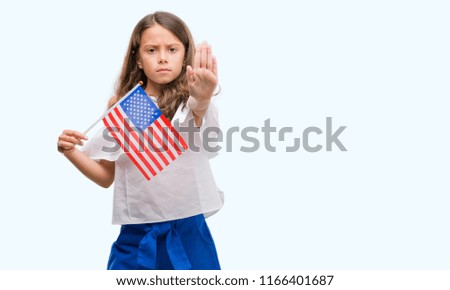 Brunette hispanic girl holding flag of United States of America with open hand doing stop sign with serious and confident expression, defense gesture
