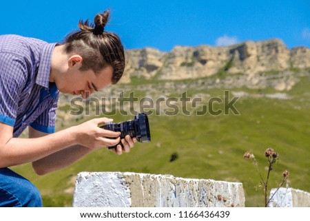 A young man in a blue shirt photographs mountains.