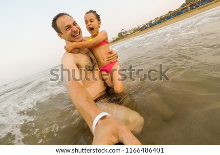 Father and daughter playing happy at a beautiful beach making selfie.