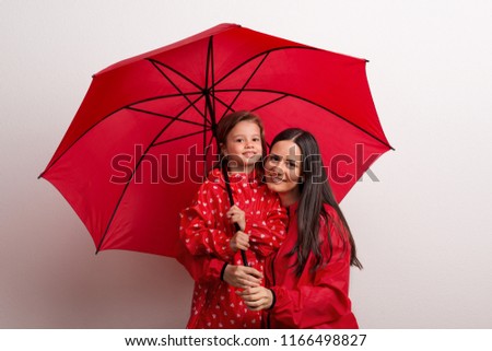 A small girl with her mother under an umbrella on a white background.