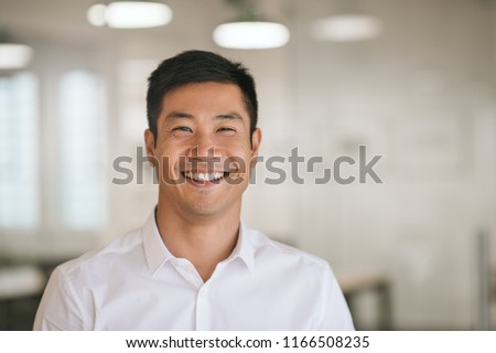 Well dressed young Asian businessman smiling confidently while standing alone in a bright modern office Royalty-Free Stock Photo #1166508235