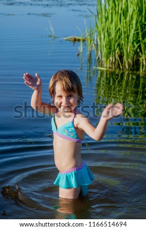 Funny little child girl go into the water of the lake to swim. Holiday, vacation and health concept.