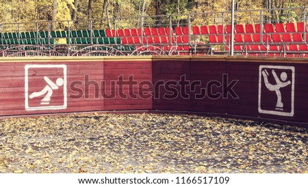 Close up on white sign or icon of skater and colored sign of the Olympic rings on a brown wooden fence in the public park.
