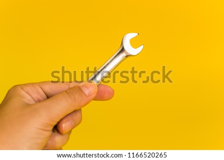 hand holding steel wrench on yellow background
