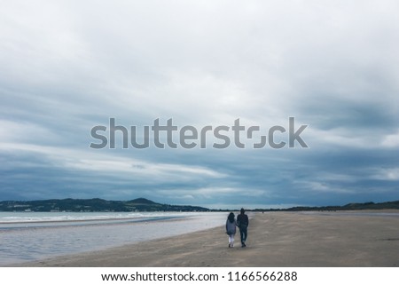 a couple walking by the sea on the beach in the evening, blue evening sky and clouds