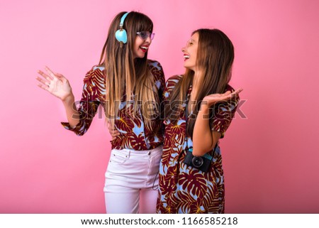 Studio positive image of tho pretty best friends woman dancing and having fun at party, cute surprised emotions, stylish color matching clothes, big headphones and vintage camera.