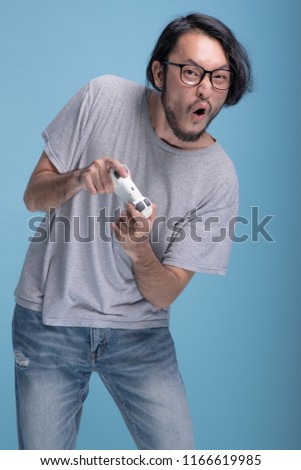 Young bearded man playing video game in blue background. Very focus Asian young hipster holding game pad having fun, half body shot. Young generation hipster relaxation concept.