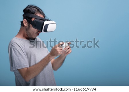 Young bearded man playing VR game in blue background. Surprise Asian young hipster wearing VR headset, half body shot. Young generation hipster relaxation concept.