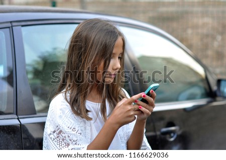Phone addicted young child, at background have a car.