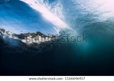 Barrel wave crashing in tropical ocean with sunlight. Underwater view