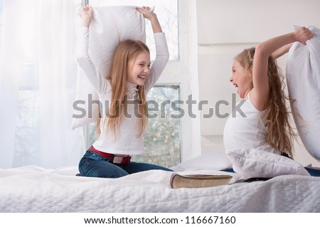 Two girls sitting pillow fight in bed. Horizontal. Royalty-Free Stock Photo #116667160