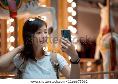 Young female photographer using smartphone in front of carousel