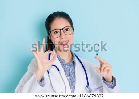young female physician showing okay sign and holding an injection in her hand with a friendly smile. 
