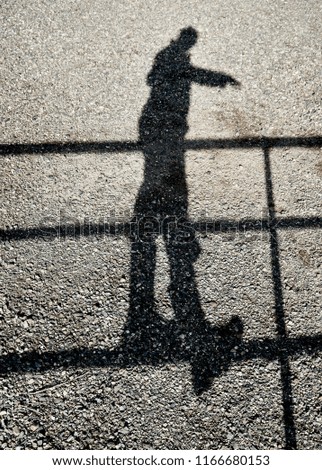 Shadow of a person balancing on one leg on a fence reflected on a gravel ground