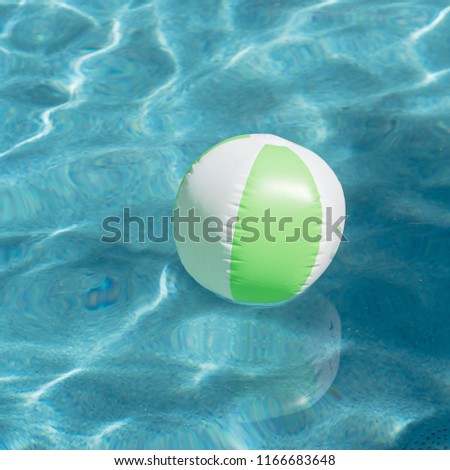 One bright green beach ball in blue swimming pool, floating in refreshing swimming pool with waves reflecting in summer sun. Active vacation background. Lifesaver for kid. Sunny day at the pool