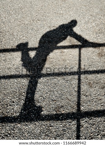 Shadow of a person climbing over a fence reflected on a gravel ground